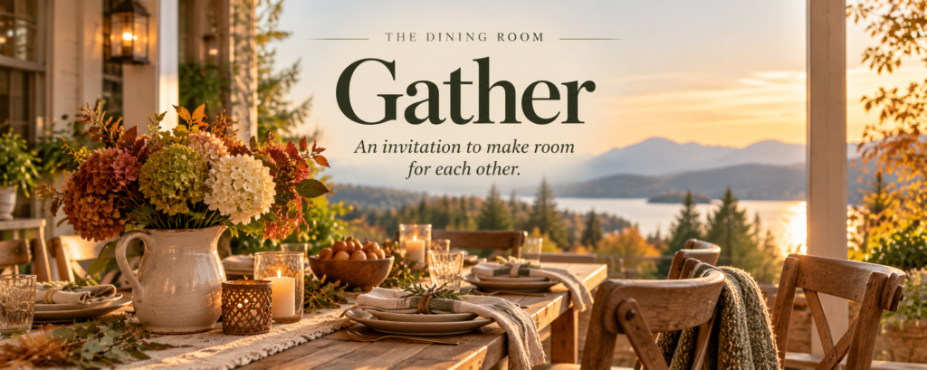 A warmly set wooden dining table with autumn flowers, candles, and linen napkins on a covered porch overlooking a lake and forested mountains at sunset.